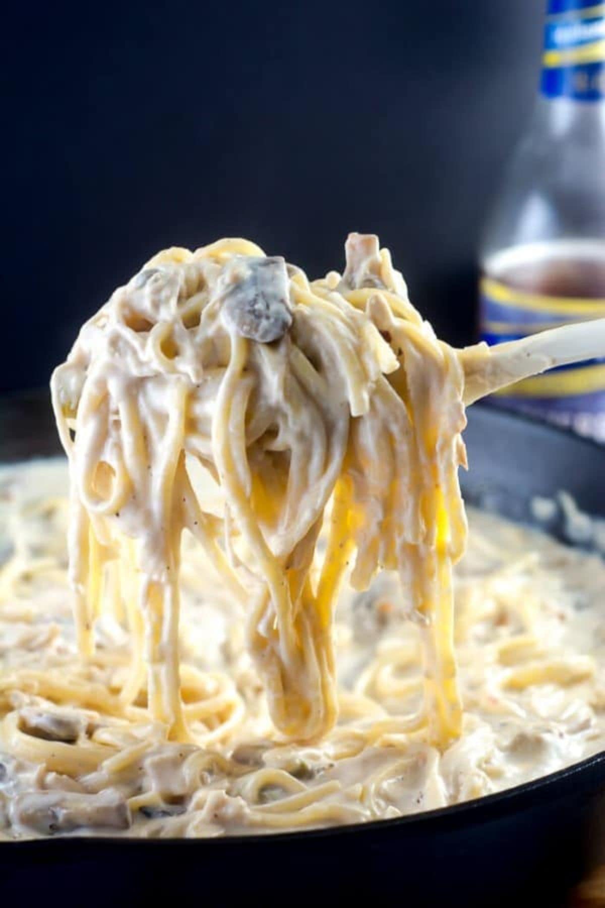 Large spoonful of chicken tetrazzini held above a cast iron skillet.