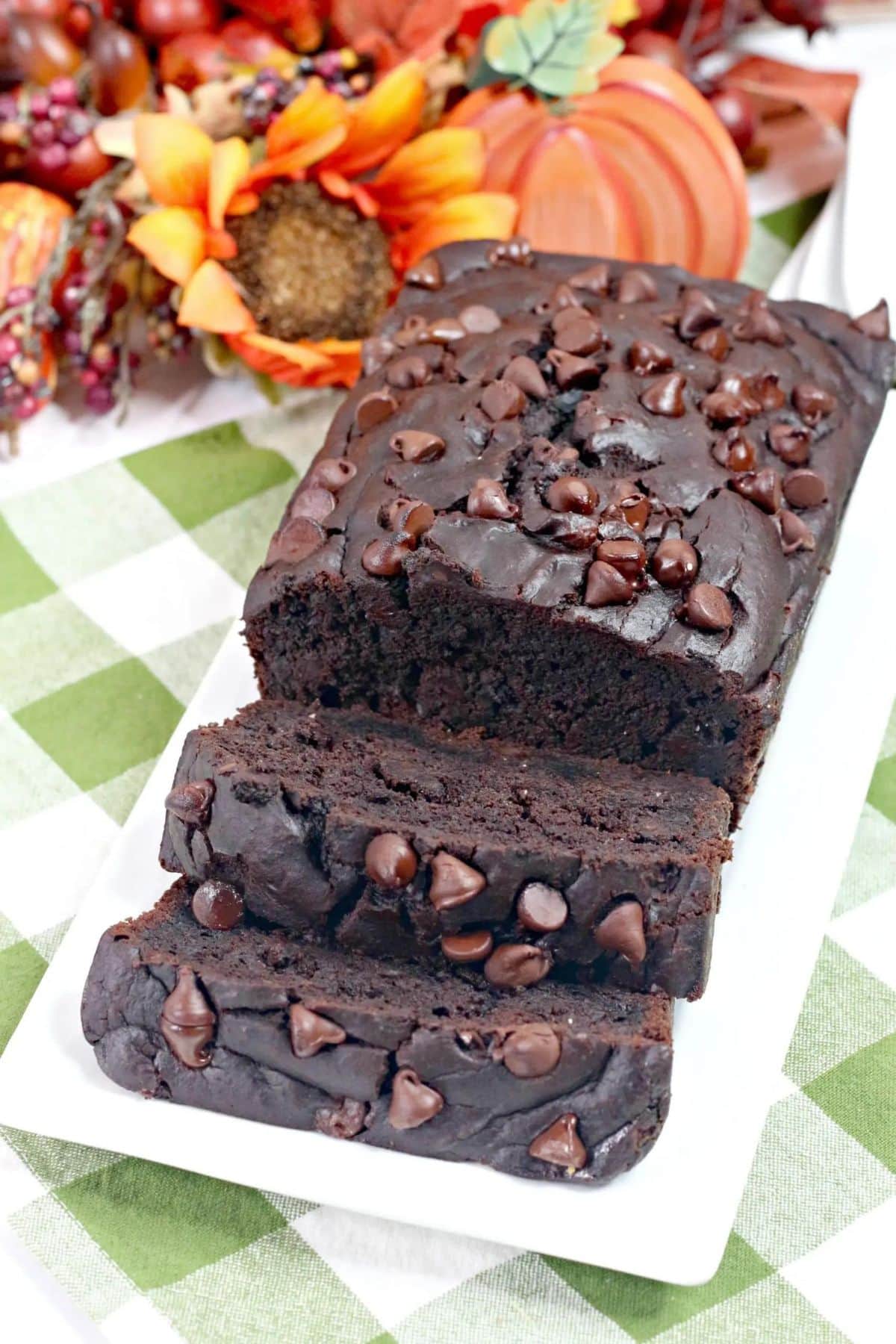 Loaf of chocolate bourbon pumpkin bread on a serving platter with two slices cut.