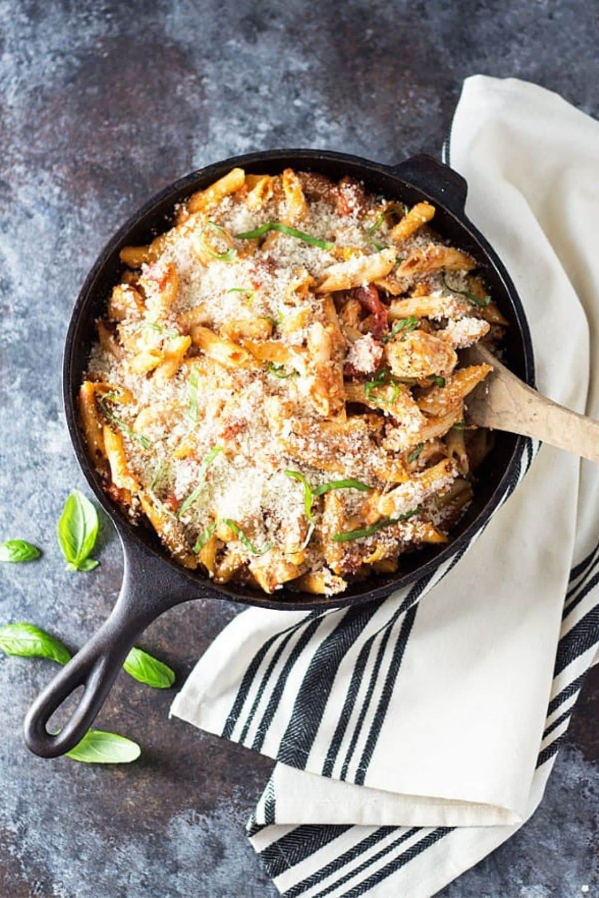 Skillet full of creamy chicken parmesan casserole with a wooden spoon in it.