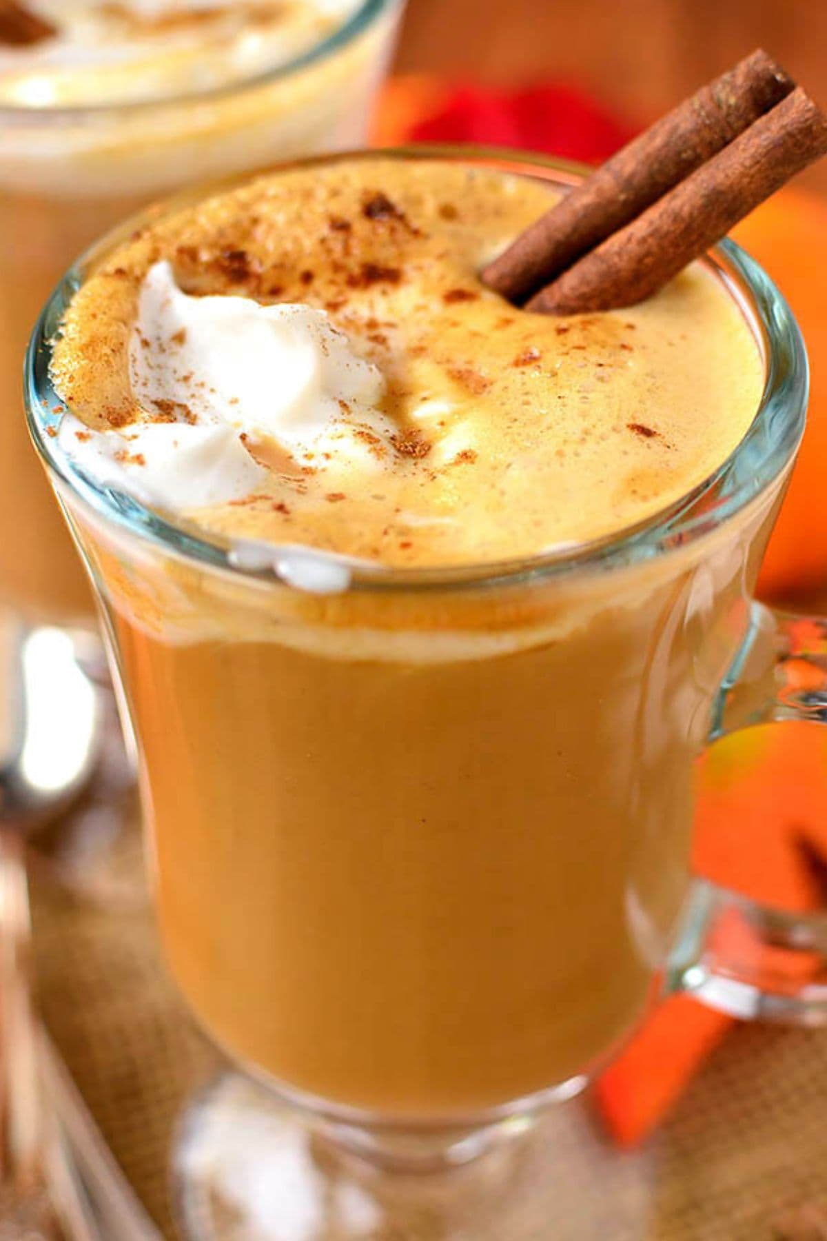 Pumpkin spiced latte in a glass mug topped with cinnamon sticks.