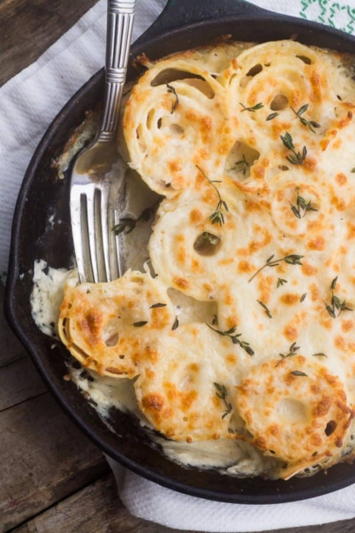 Skillet full of ham and swiss pasta roll-up gratin with a piece missing.