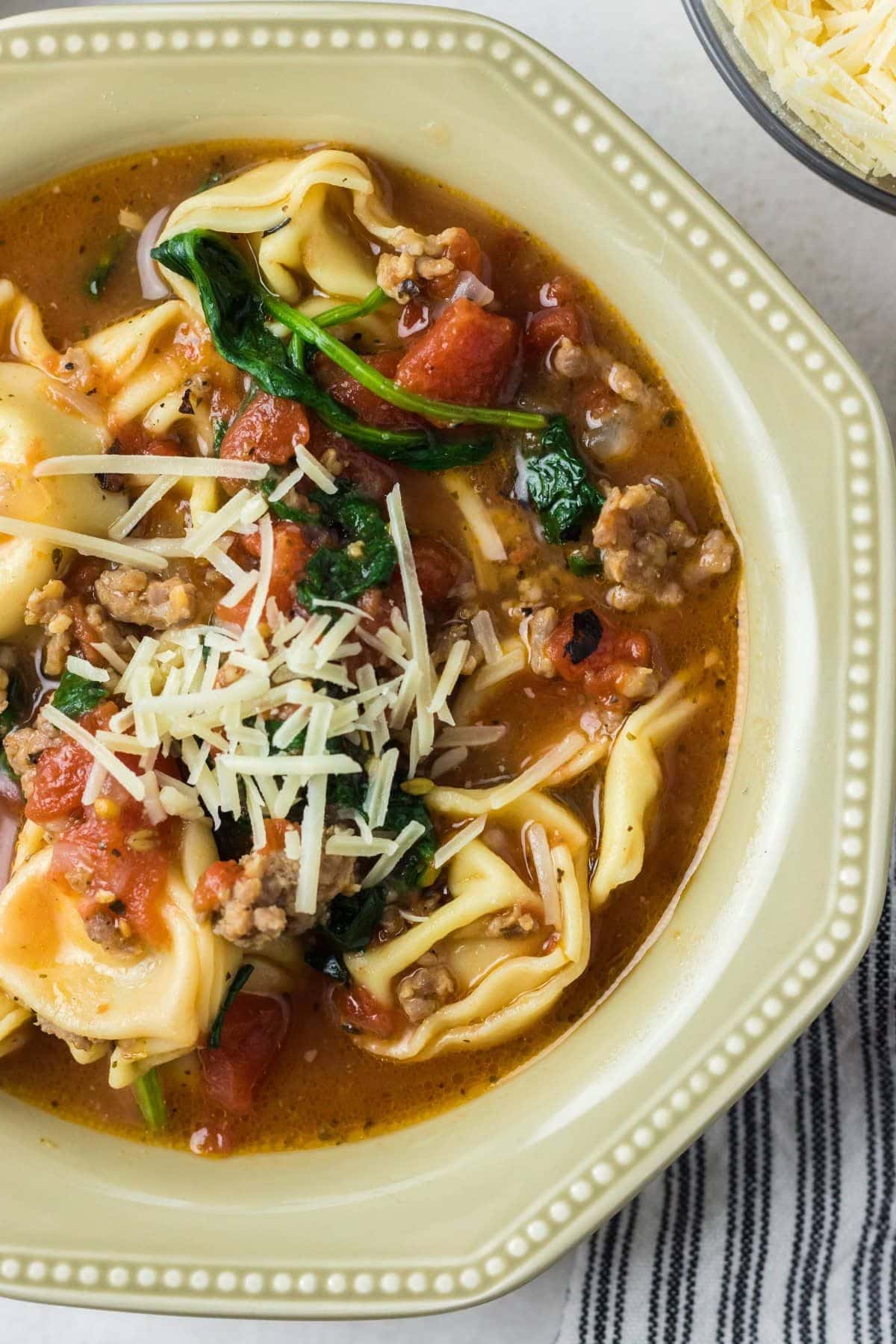 Bowl full of intant pot tortellini soup topped with parmesan cheese.