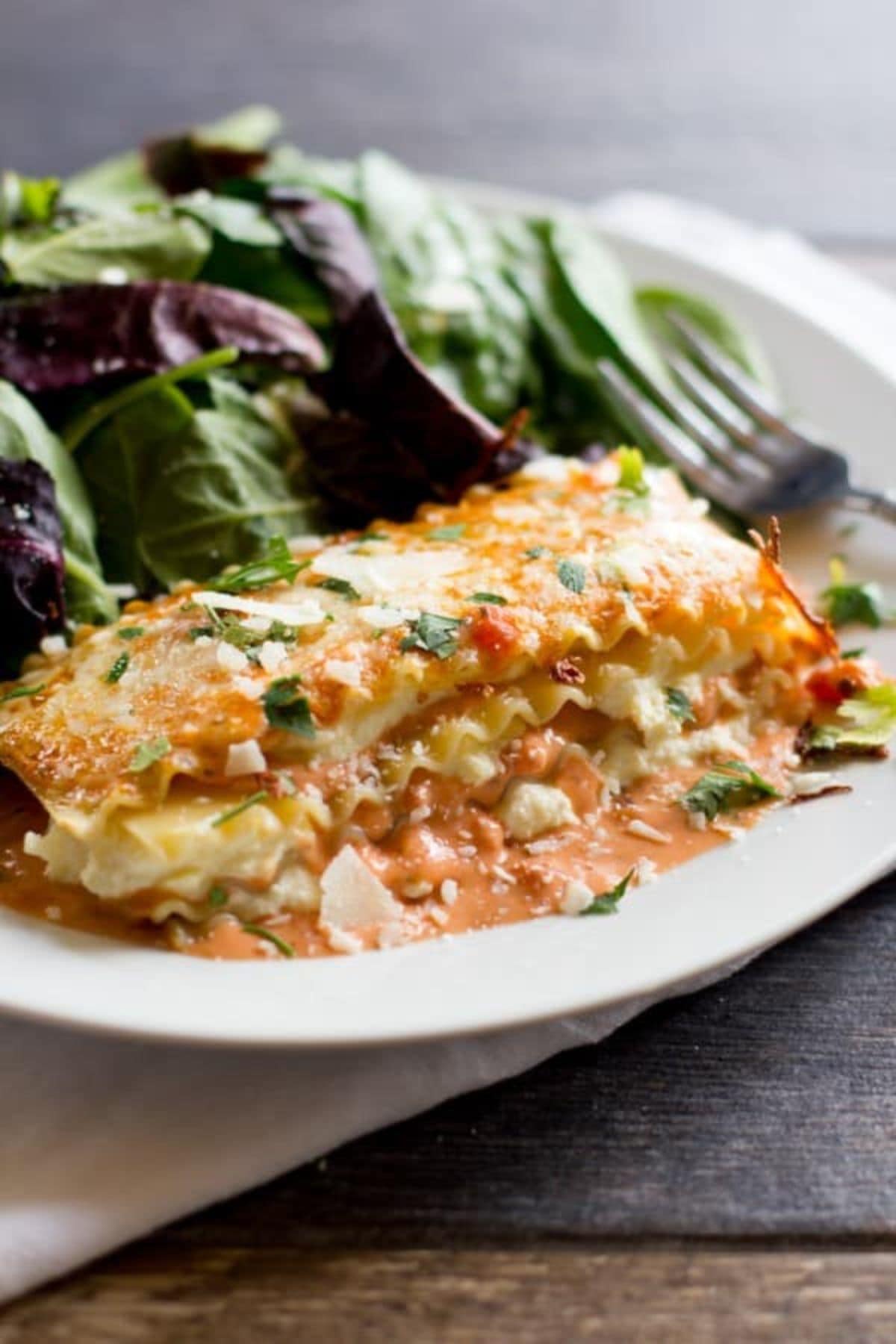 Slice of lasagna rose and a salad on a plate with a fork.