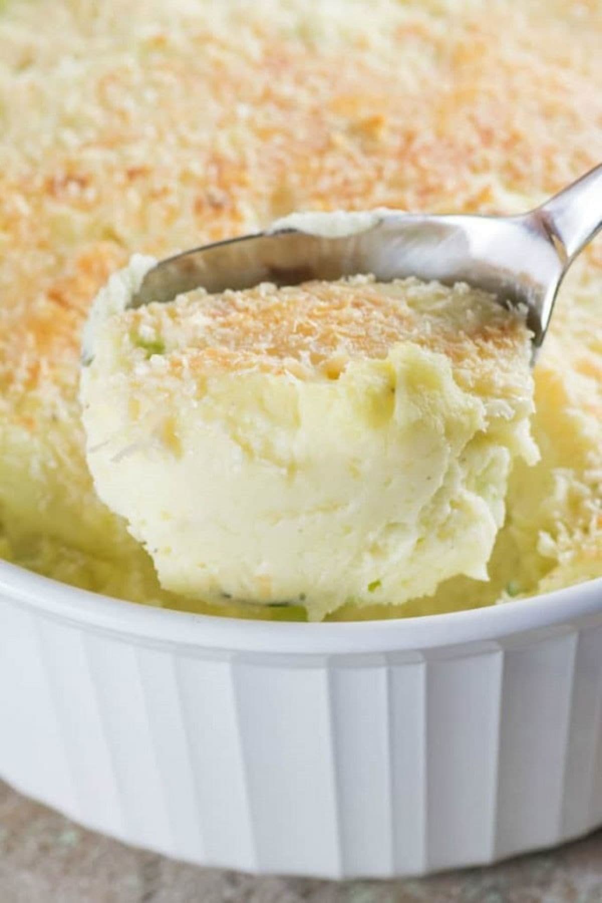 Scoop of mashed potato casserole being removed from a casserole dish.