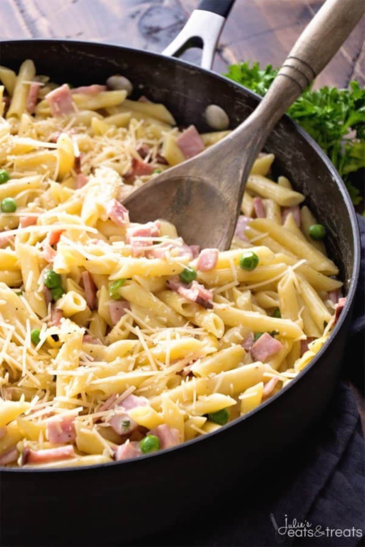 Ham and penne in a skillet with a wooden spoon.