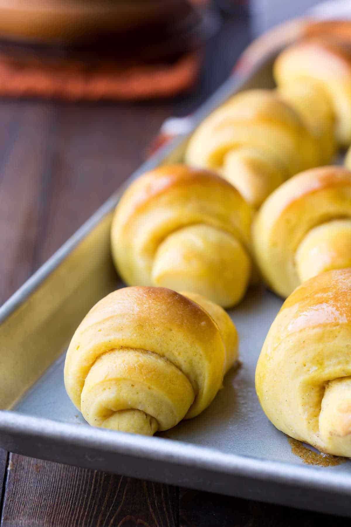 Pumpkin crescent rolls on a stainless steel baking sheet.