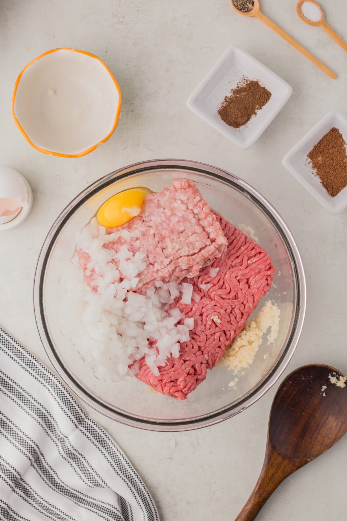 Egg, onions, beef, pork, and breadcrumbs added to a bowl. 