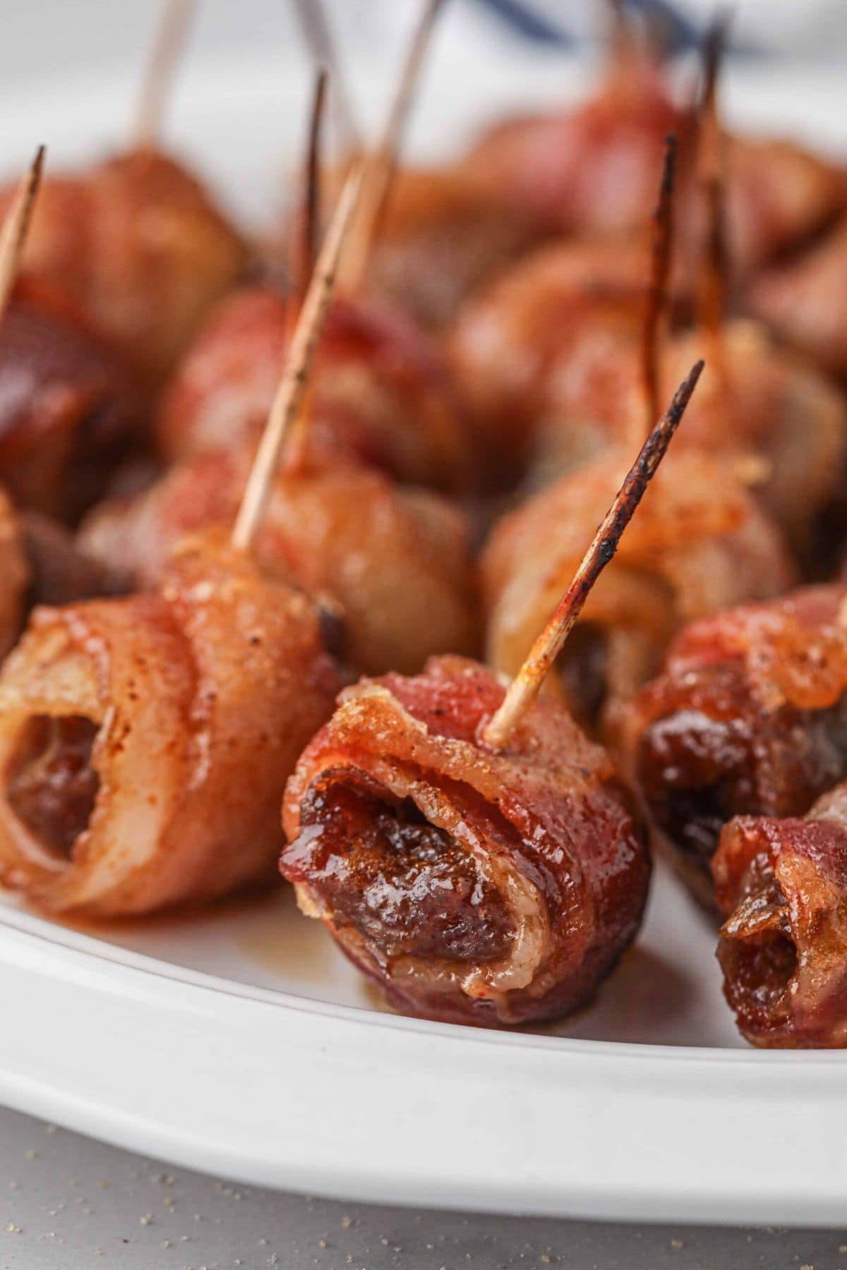 Bacon wrapped dates with toothpicks inside them, on a platter ready to serve.