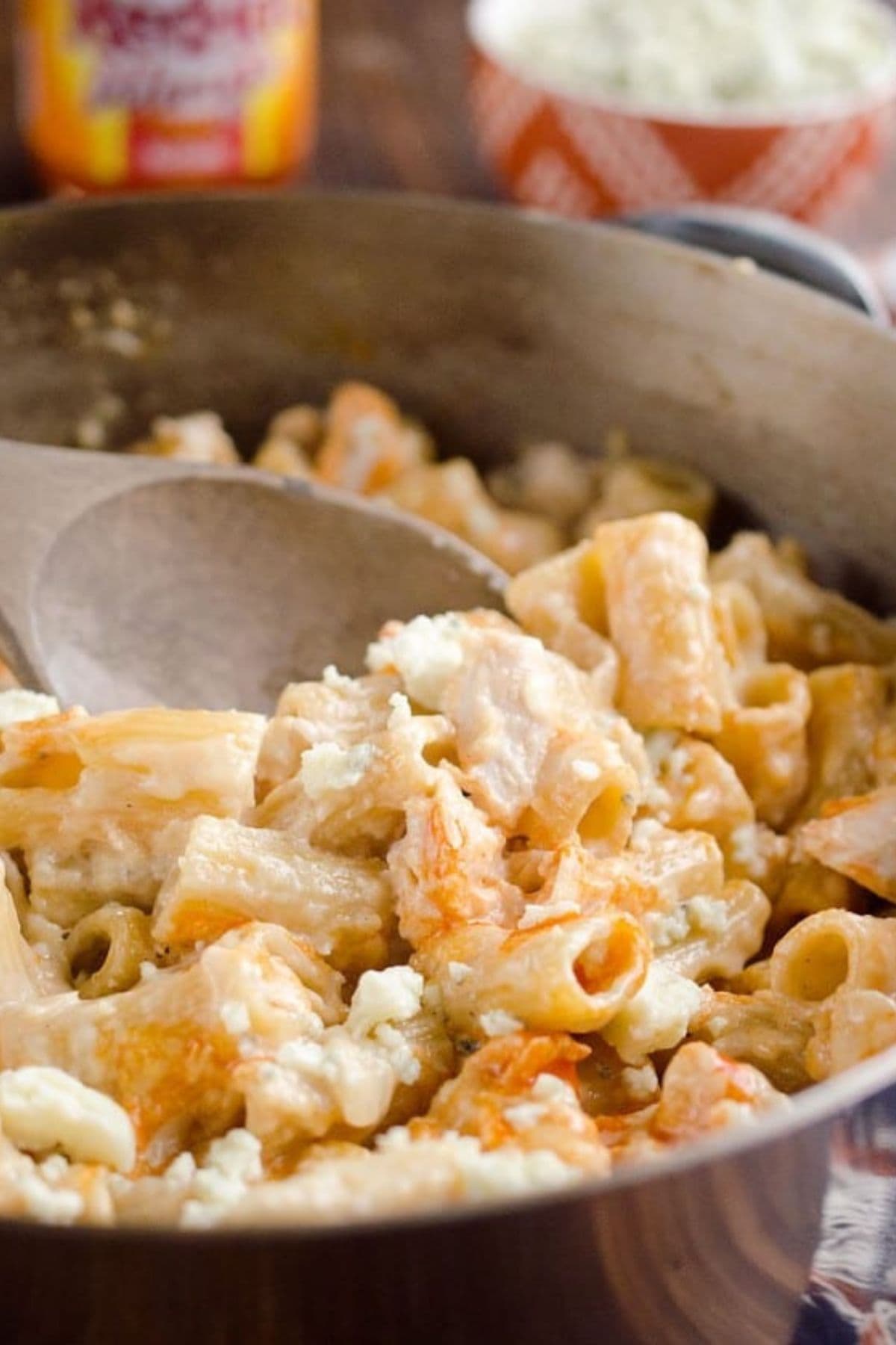 Buffalo chicken pasta being removed from a sauce pan with a wooden spoon.