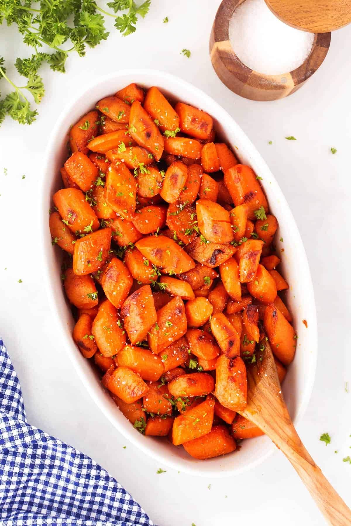 Caramelized carrots in a serving dish with a wooden spoon.