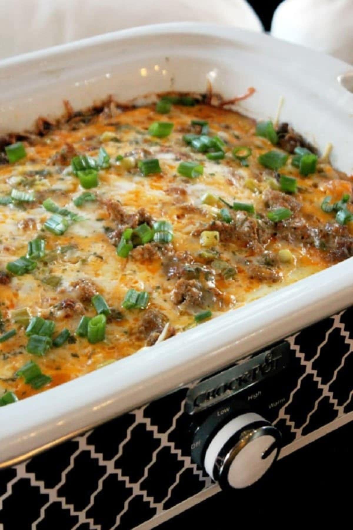 Slow cooker full of sausage casserole and garnished with sliced green onions.