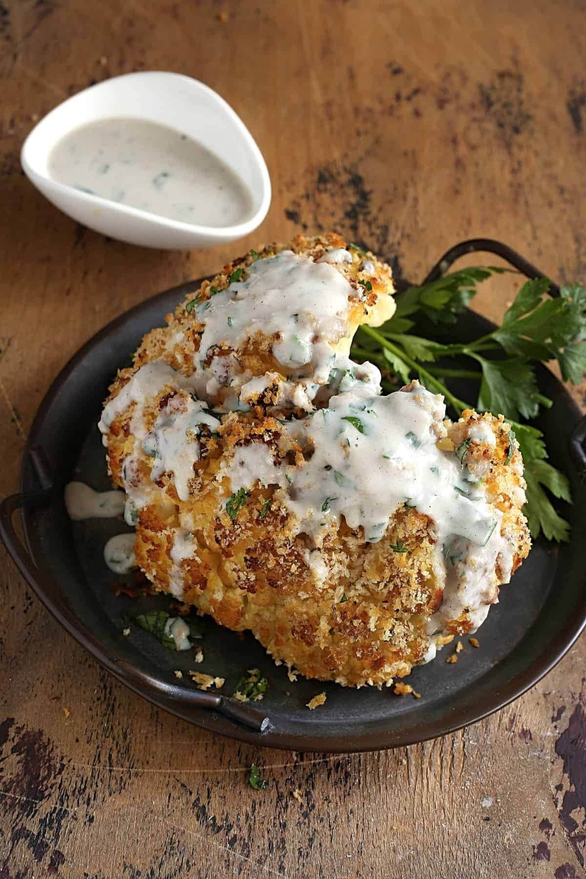 Head of roasted cauliflower on a plate with some fresh parsley.