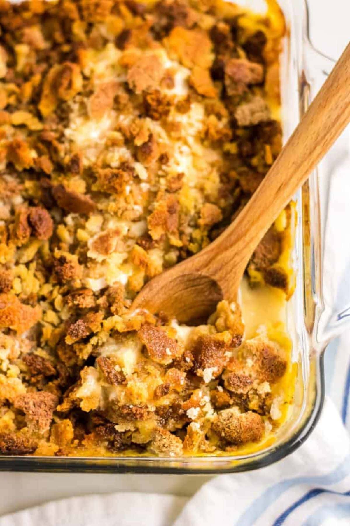 Wooden spoonful of chicken stuffing casserole being removed from the baking dish.