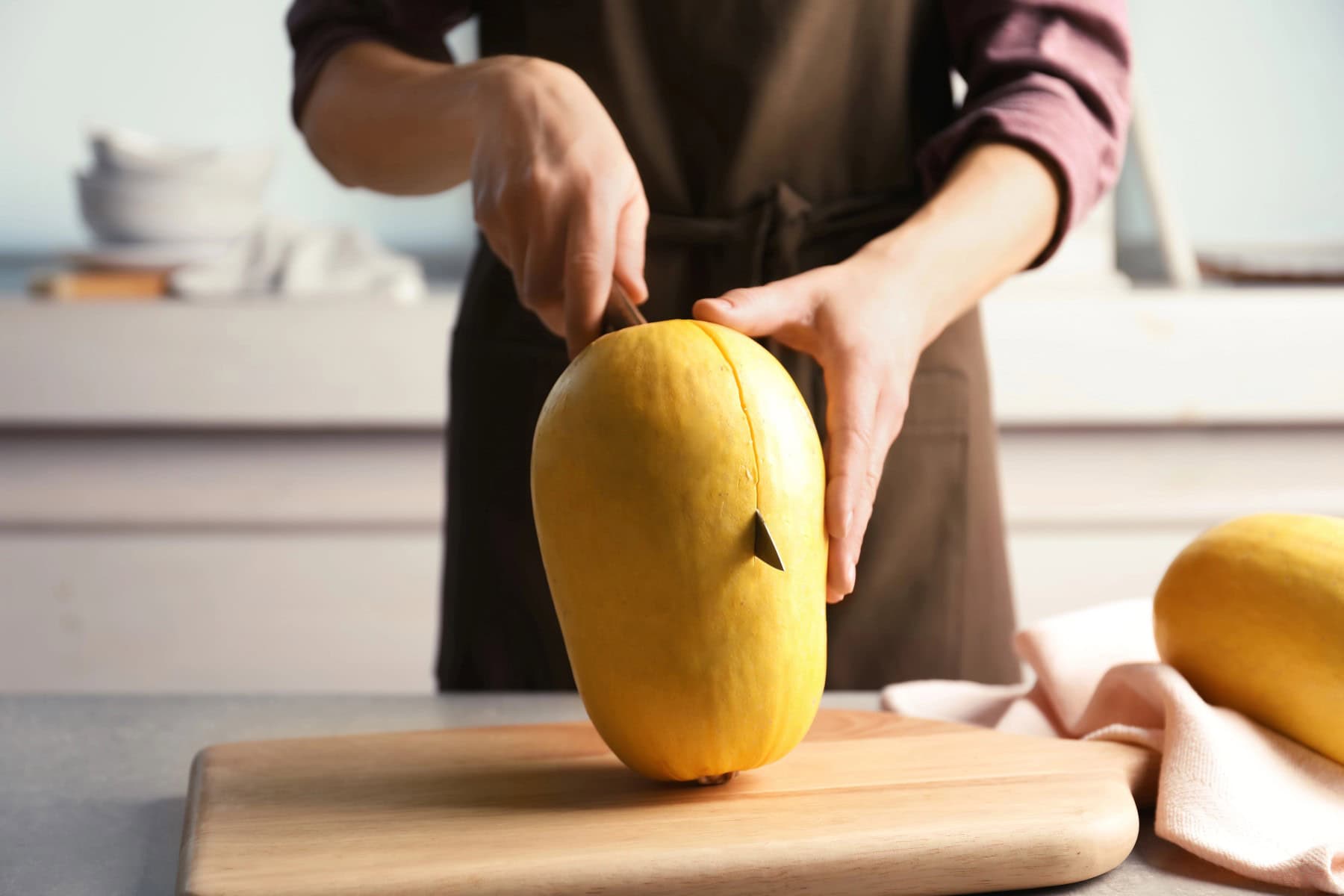 Woman cutting spaghetti squash on table in kitchen, closeup.