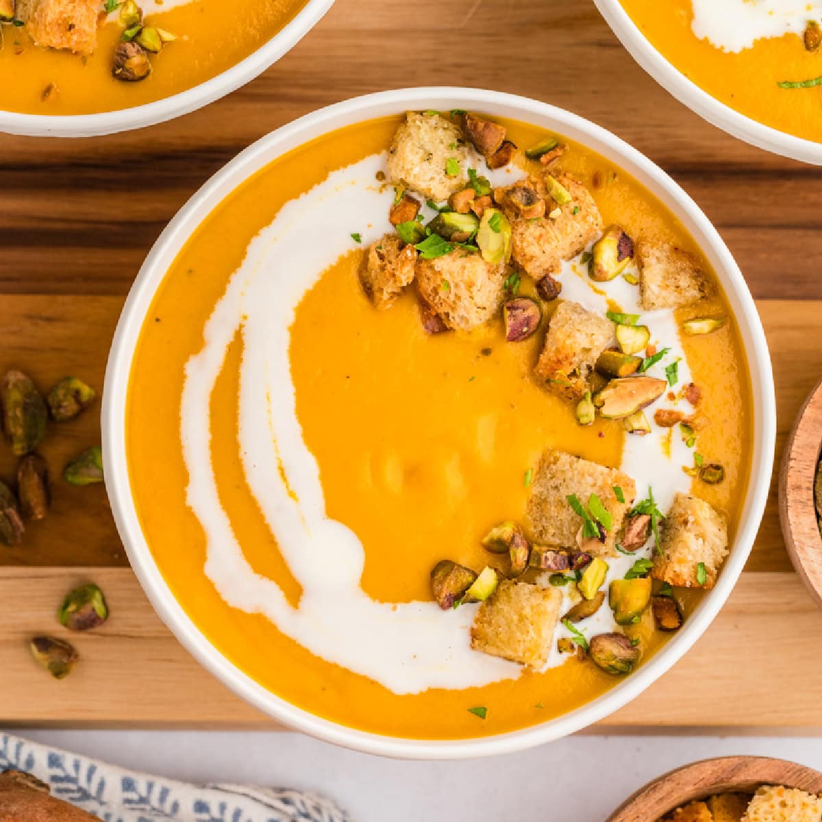 Square photo of a bowl of soup with garnish and coconut milk drizzle. 