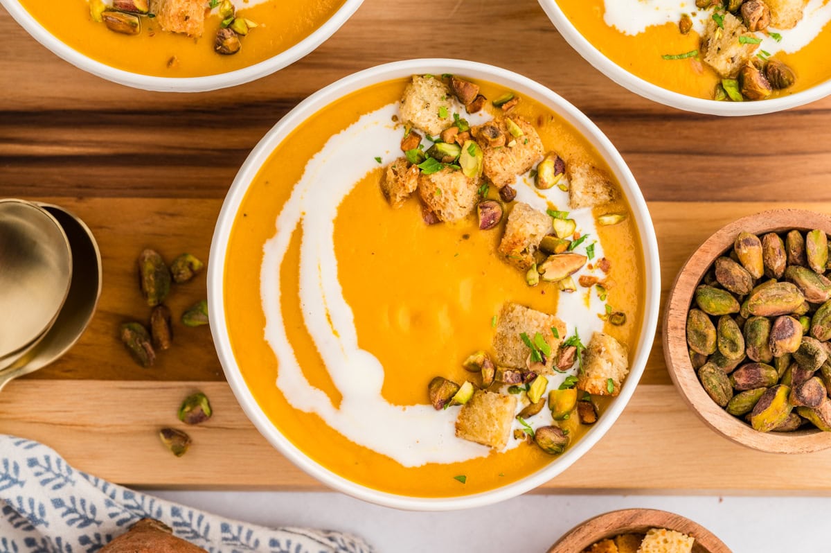 Horizontal photo overhead of a bowl  of soup with garnish and pistachios beside the bowl. 