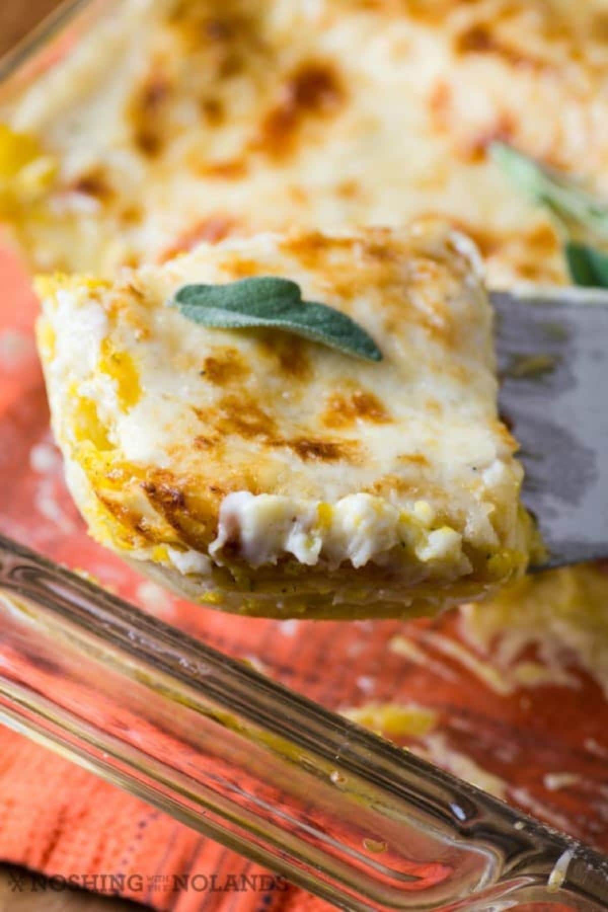 Slice butternut squash lasagna on a spatula held in the air above a casserole dish.