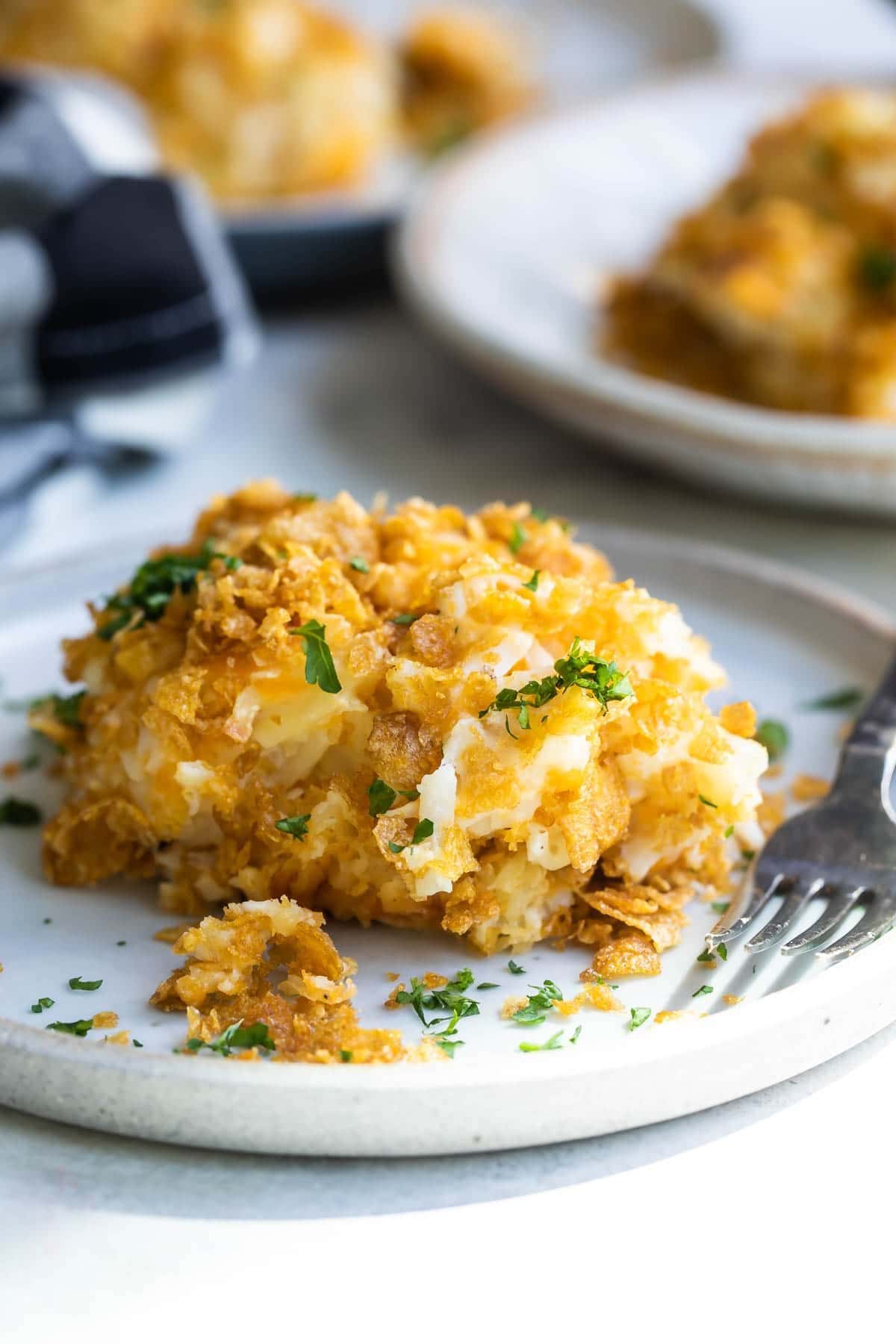 Scoop of cheesy potato casserole on a plate and garnished with fresh parsley.