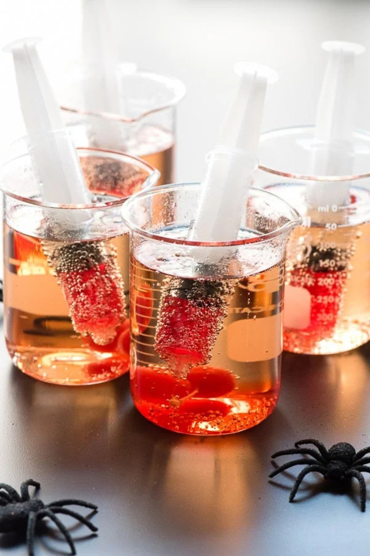 Beakers full of creepy shirley temples and syringes on a backdrop.