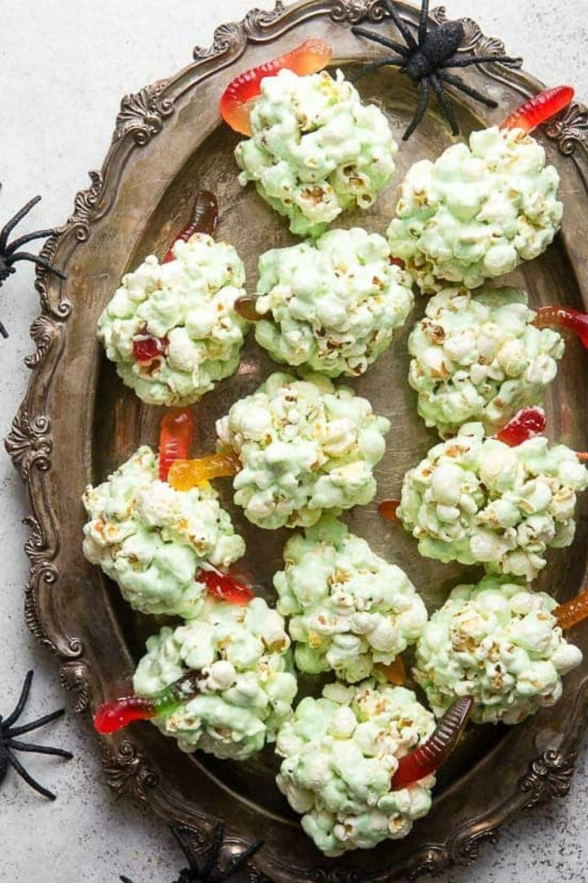 Green popcorn balls on a serving platter with grummy worms coming out of them.