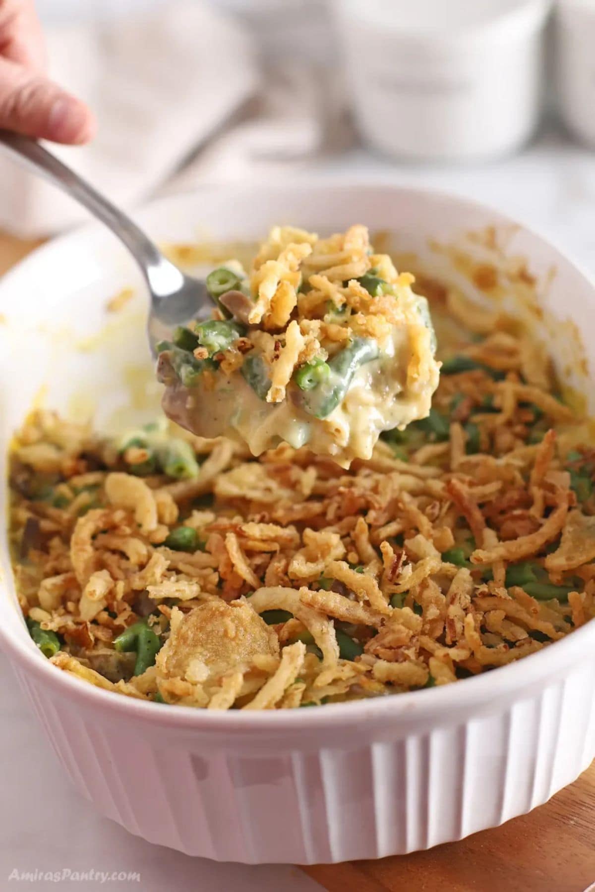 Spoonful of green bean casserole held above a full casserole dish.