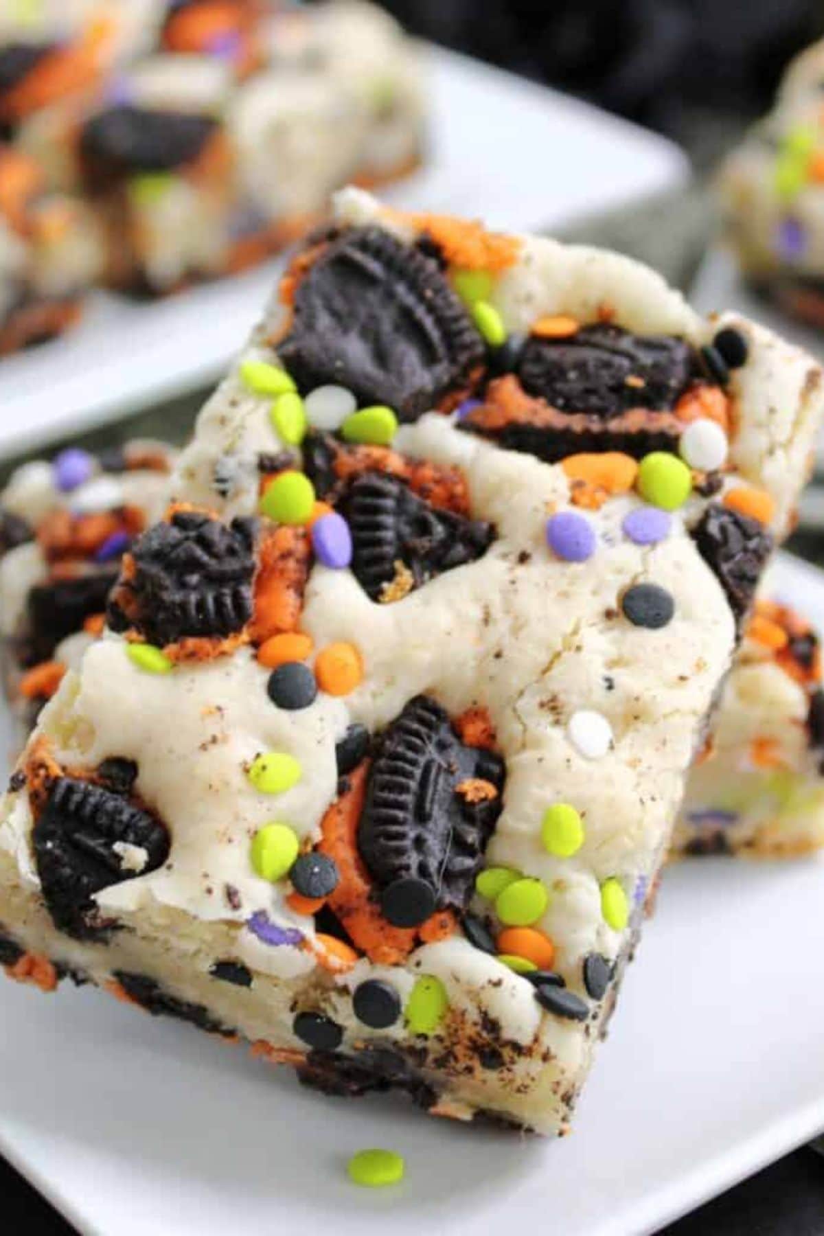 Two halloween cake bars topped with Oreo pieces and sprinkles on a plate.