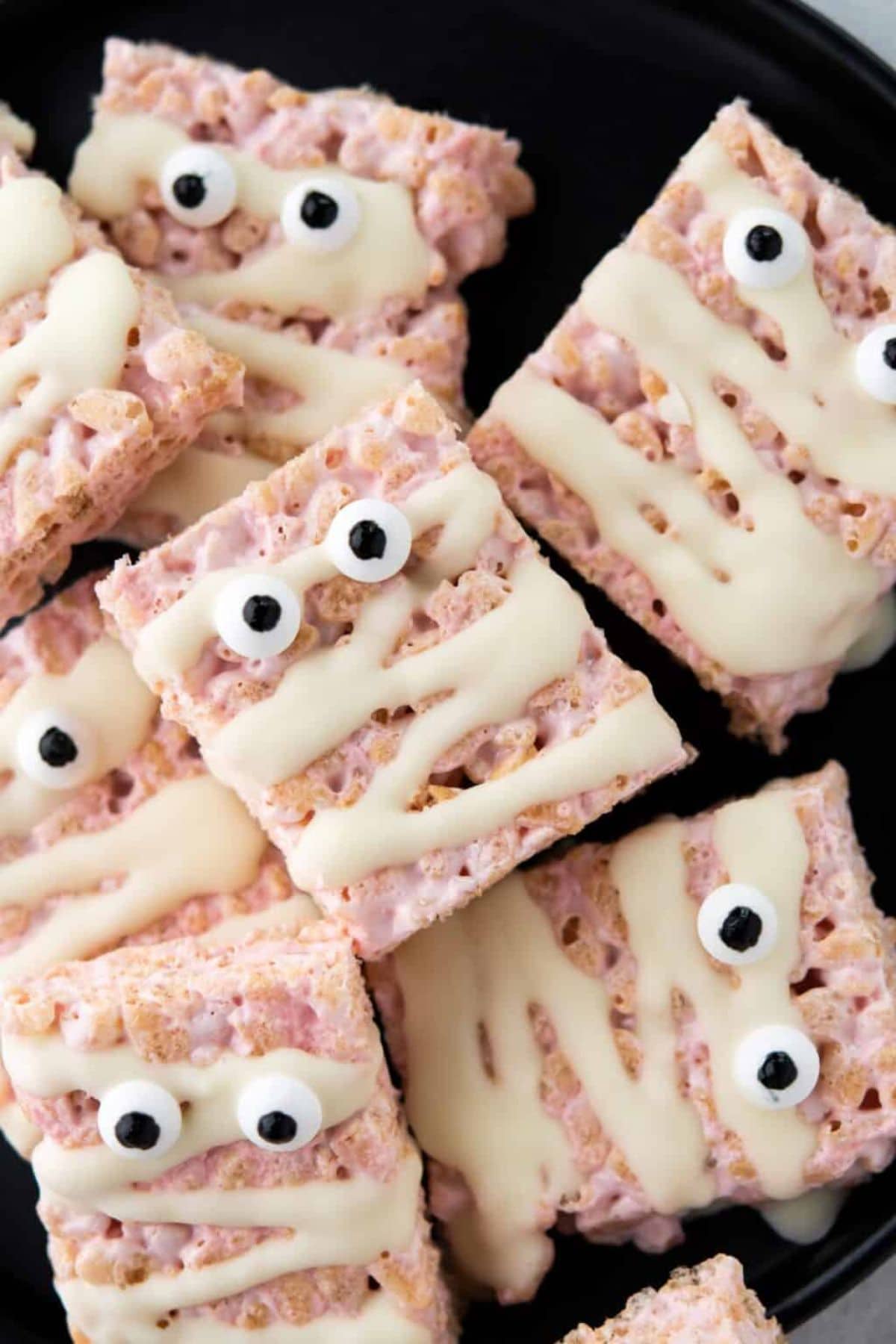 Mummy face rice krispie treats stacked in a pyramid on a serving tray.