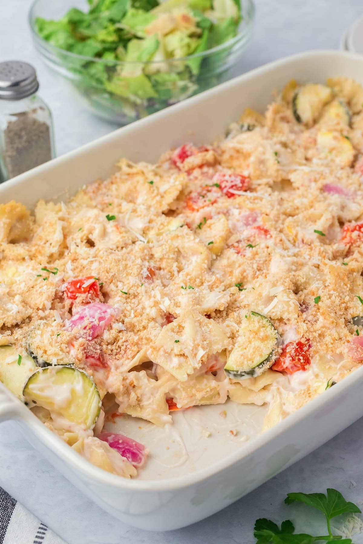 Casserole dish full of pasta primvara on a counter, with one serving removed.