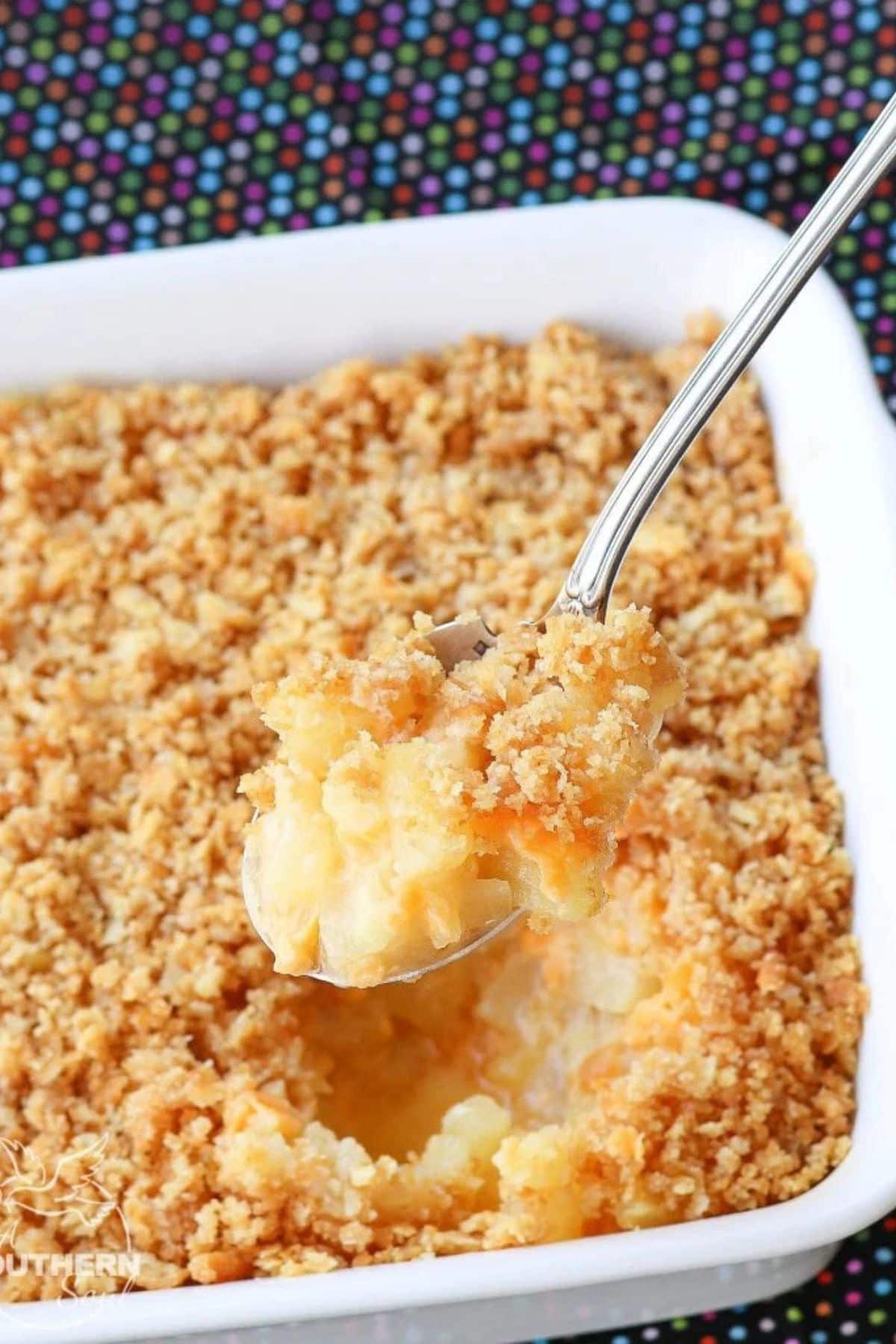 Spoonful of pineapple casserole held above a full casserole dish.