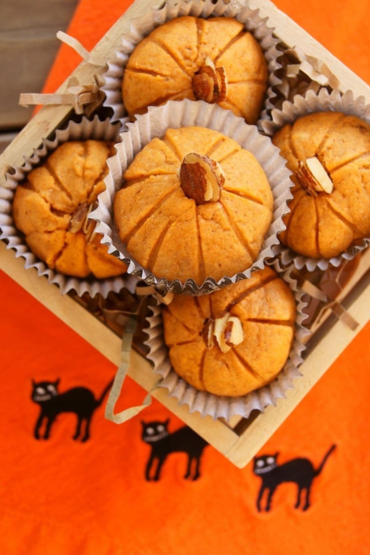 Five pumpkin almond cookies stacked in a pyramid in a small wooden box.