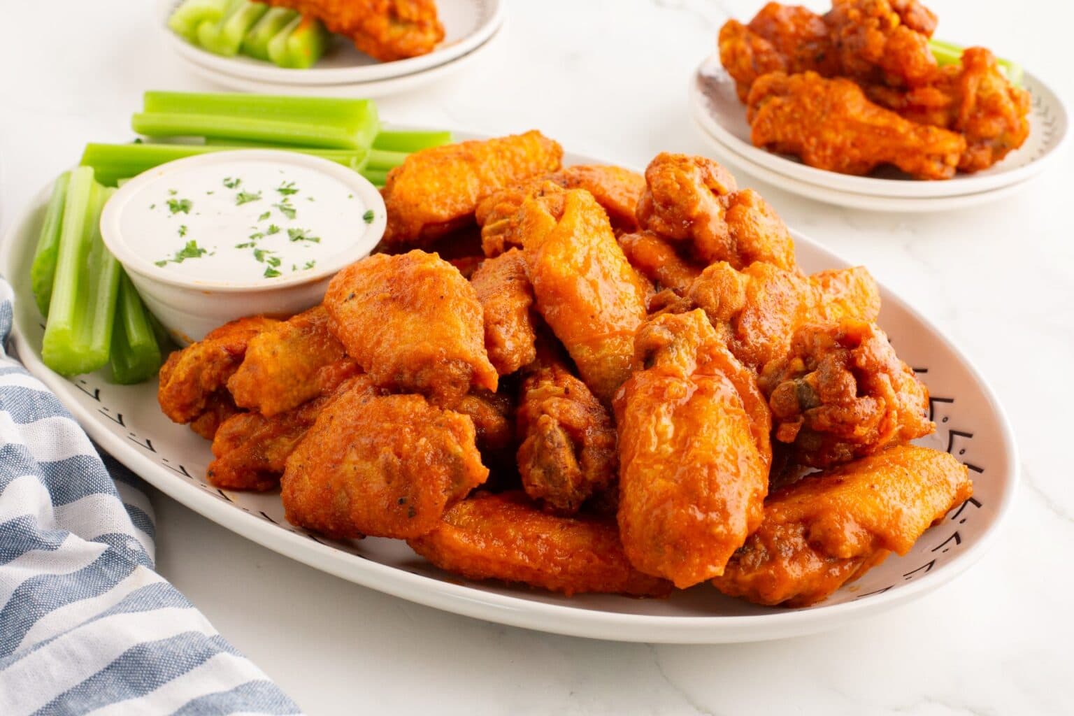 A platter of spicy chicken wings with celery sticks and ranch dipping sauce, garnished with parsley, served on a white dish.