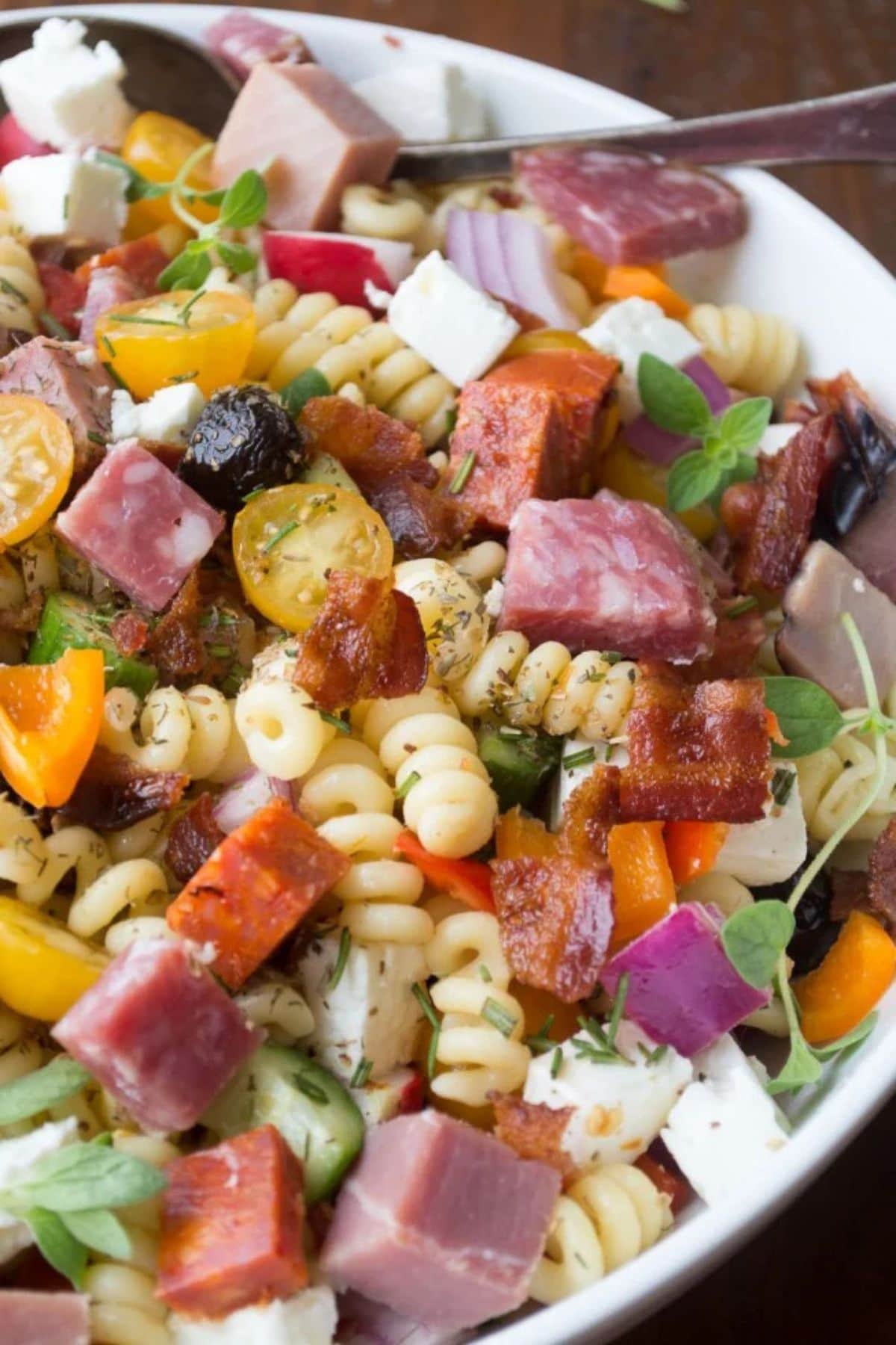 Get outside and enjoy the day with these 50 Picnic Basket Essentials. There is something for everyone to pack the perfect picnic and enjoy family time and the great outdoors. White bowl full of meat lovers pasta salad.