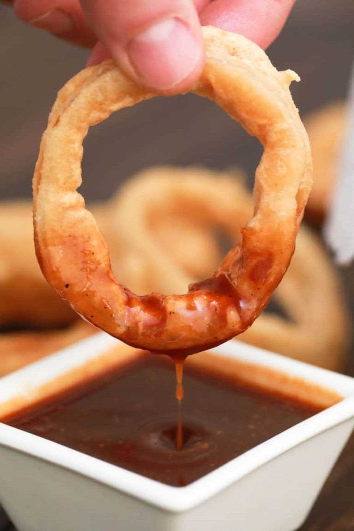 Onion ring being dipped in sauce.