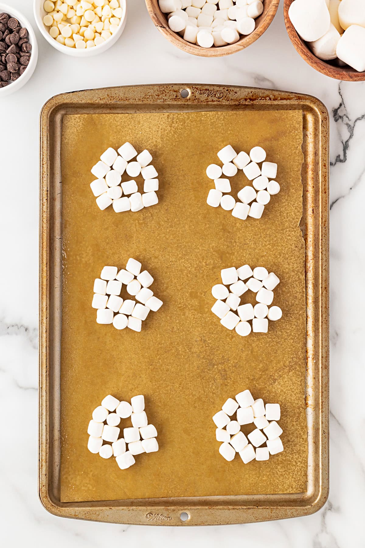 Small marshmallows in groups on a parchment lined baking sheet. 
