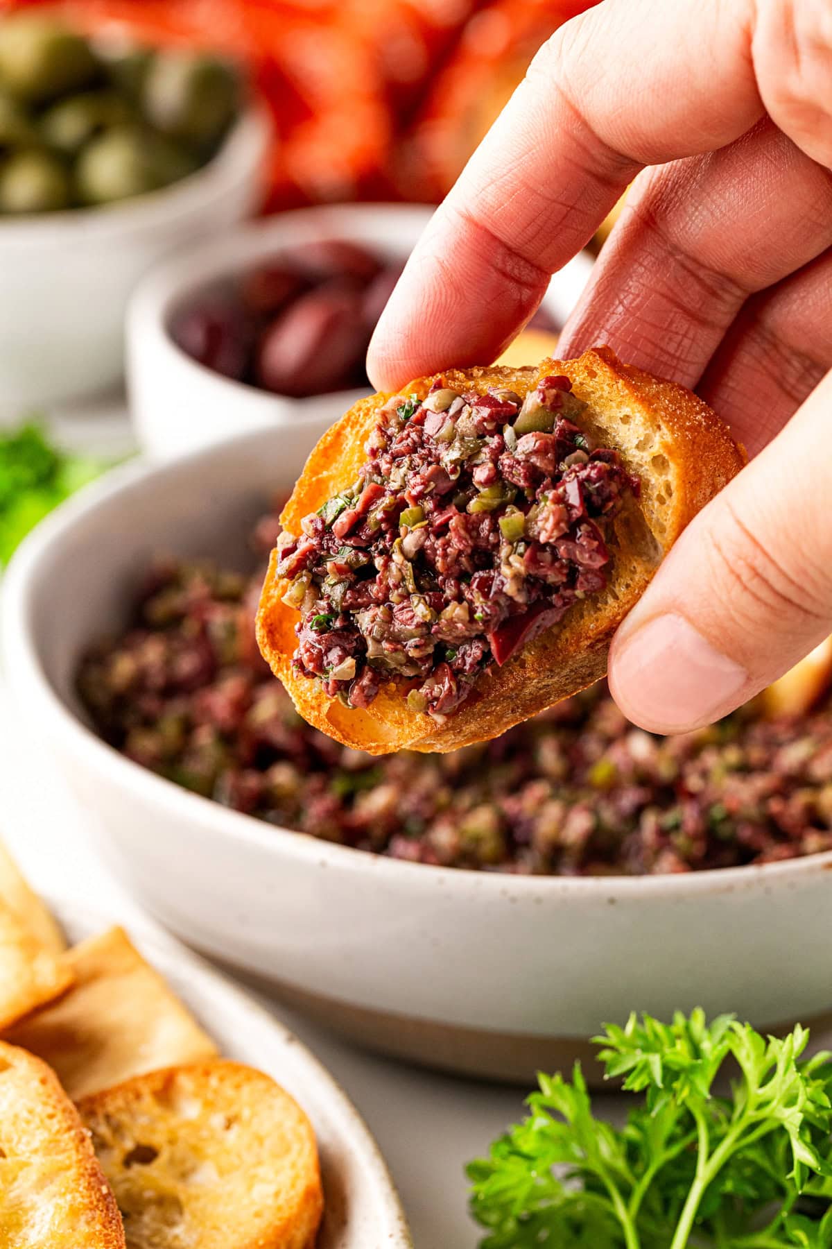 Holding a crostini with olive tapenade.