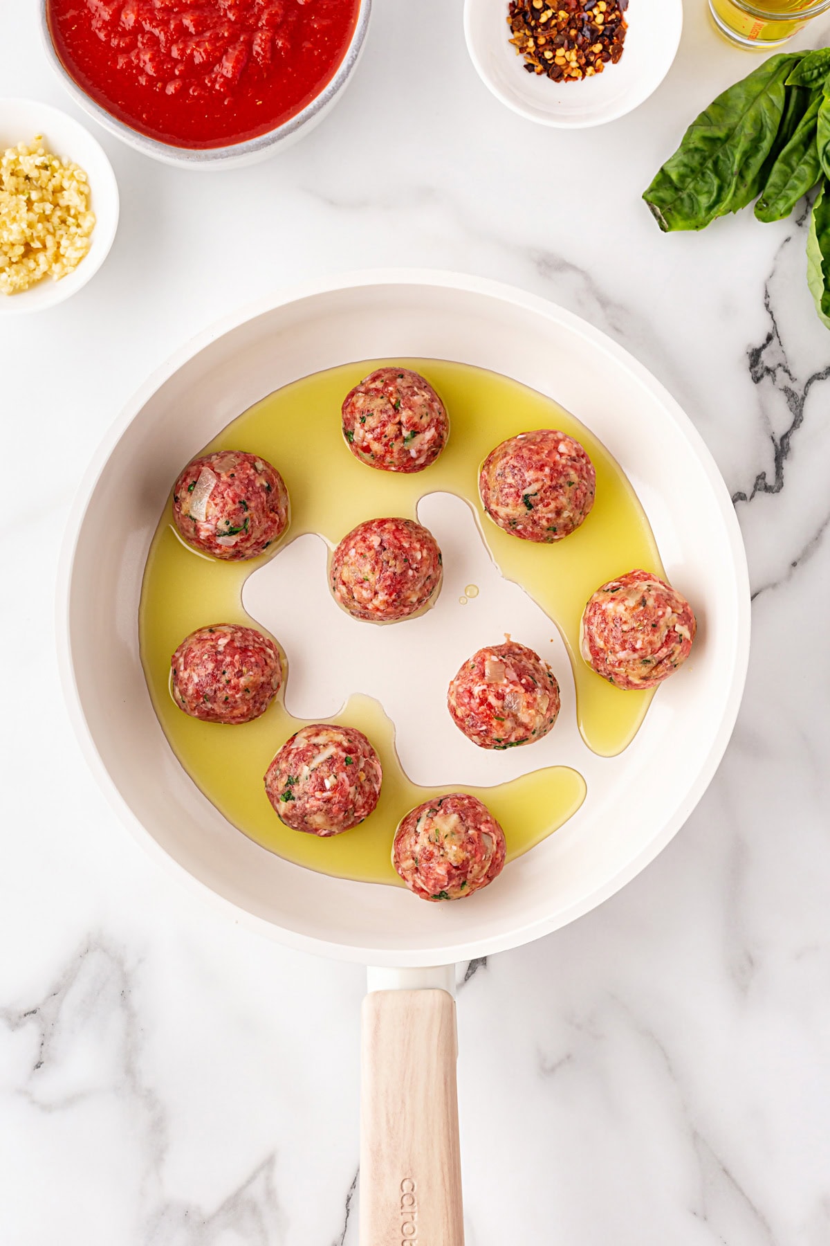 Meatballs added to a fry pan with oil. 