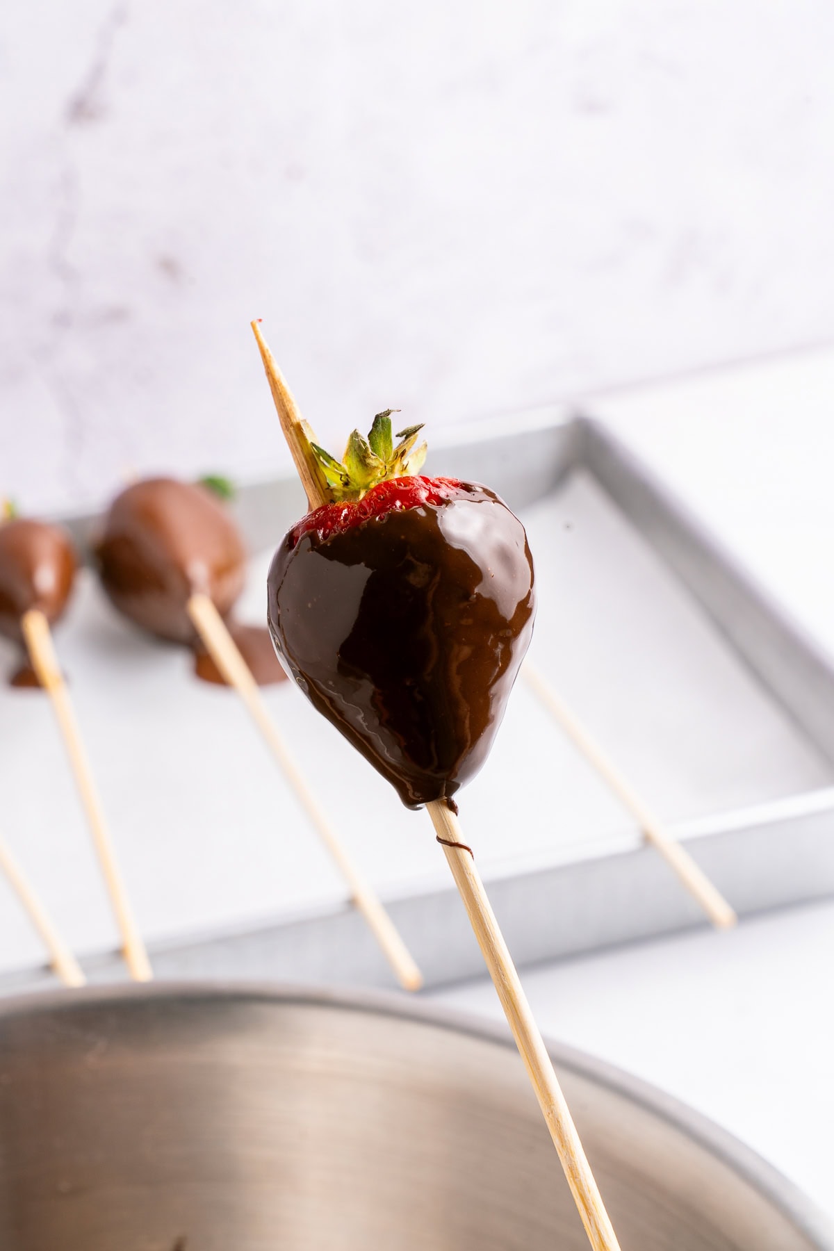 Sticking chocolate covered strawberry on a wooden skewer.