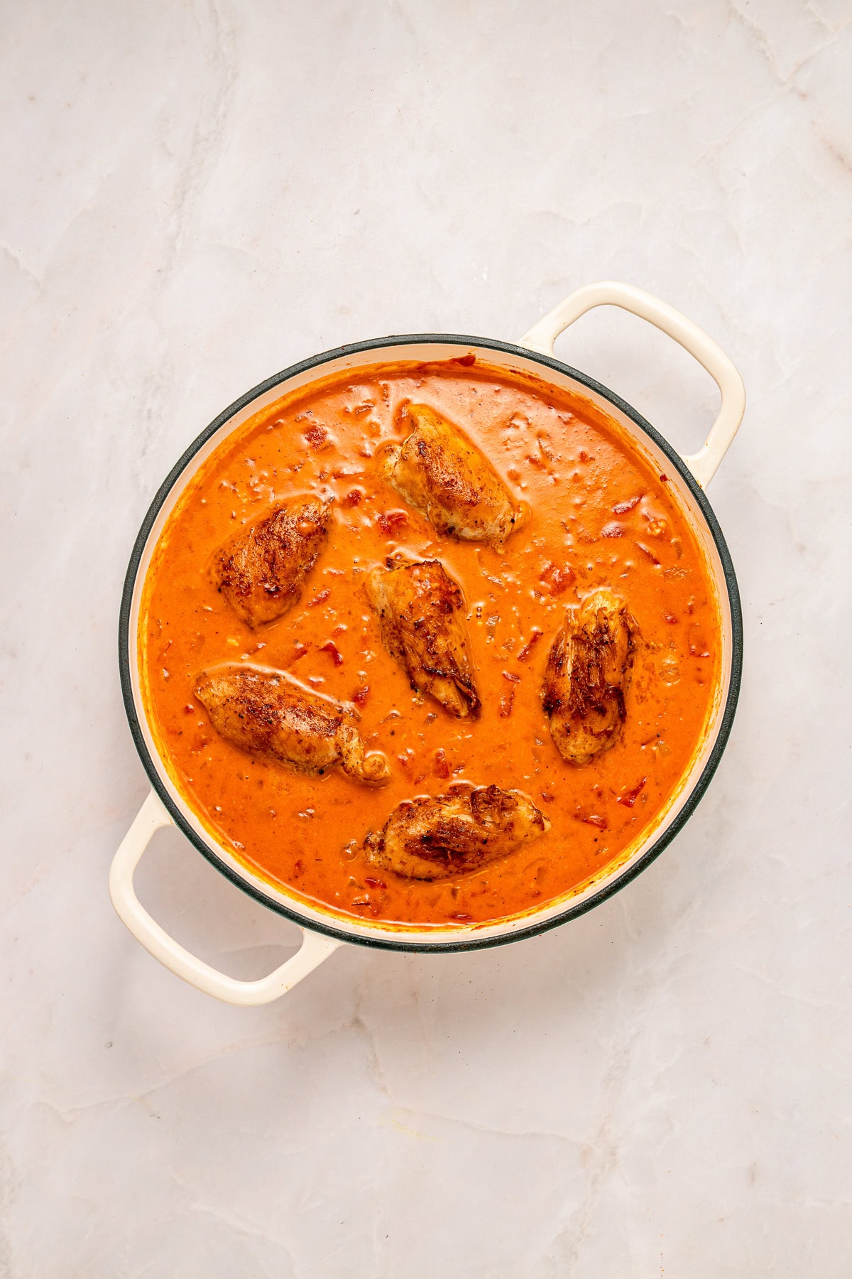 Chicken thighs simmering in creamy tomato sauce.