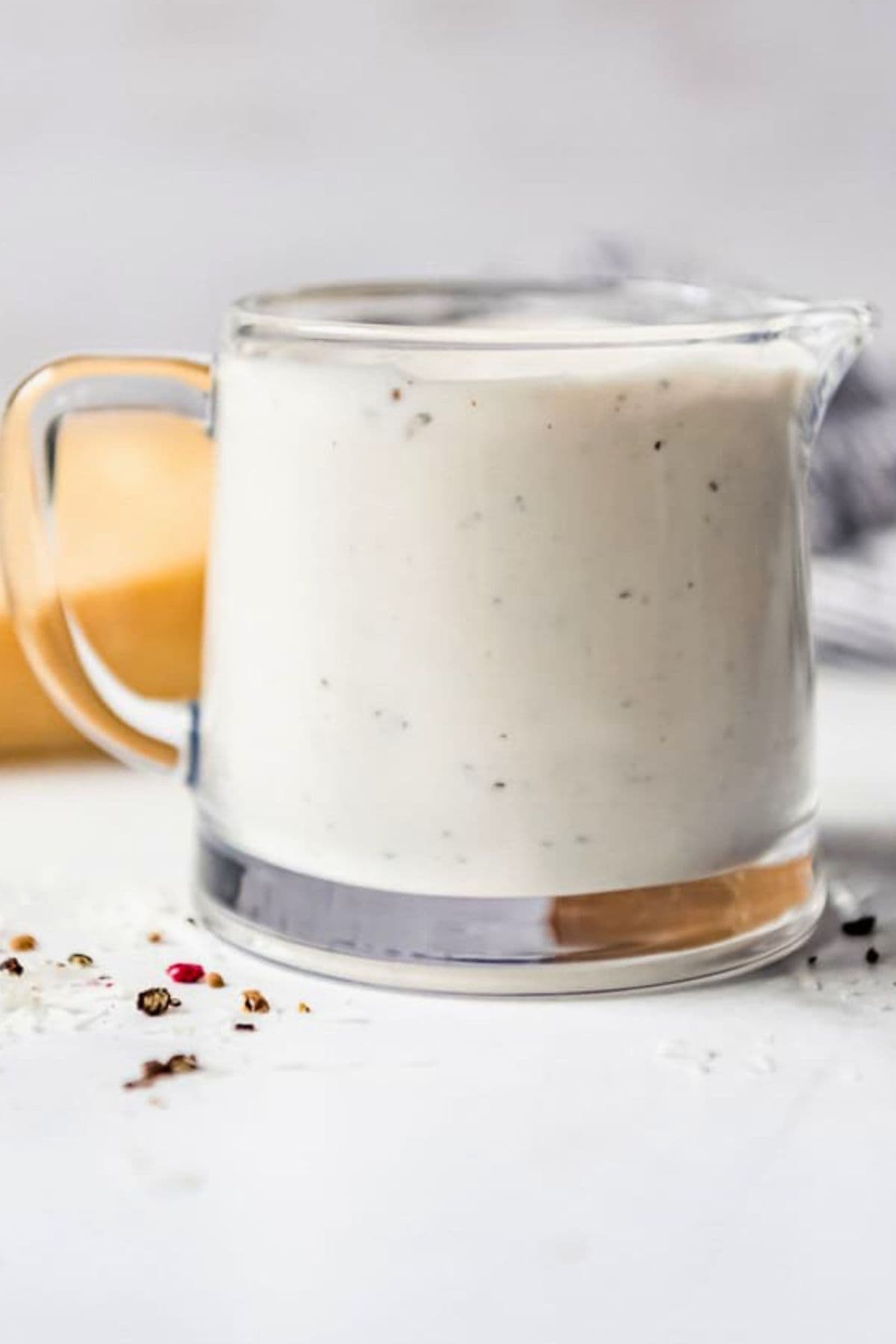 A glass pitcher filled with parmesan peppercorn dressing next to a wedge of parmesan cheese.