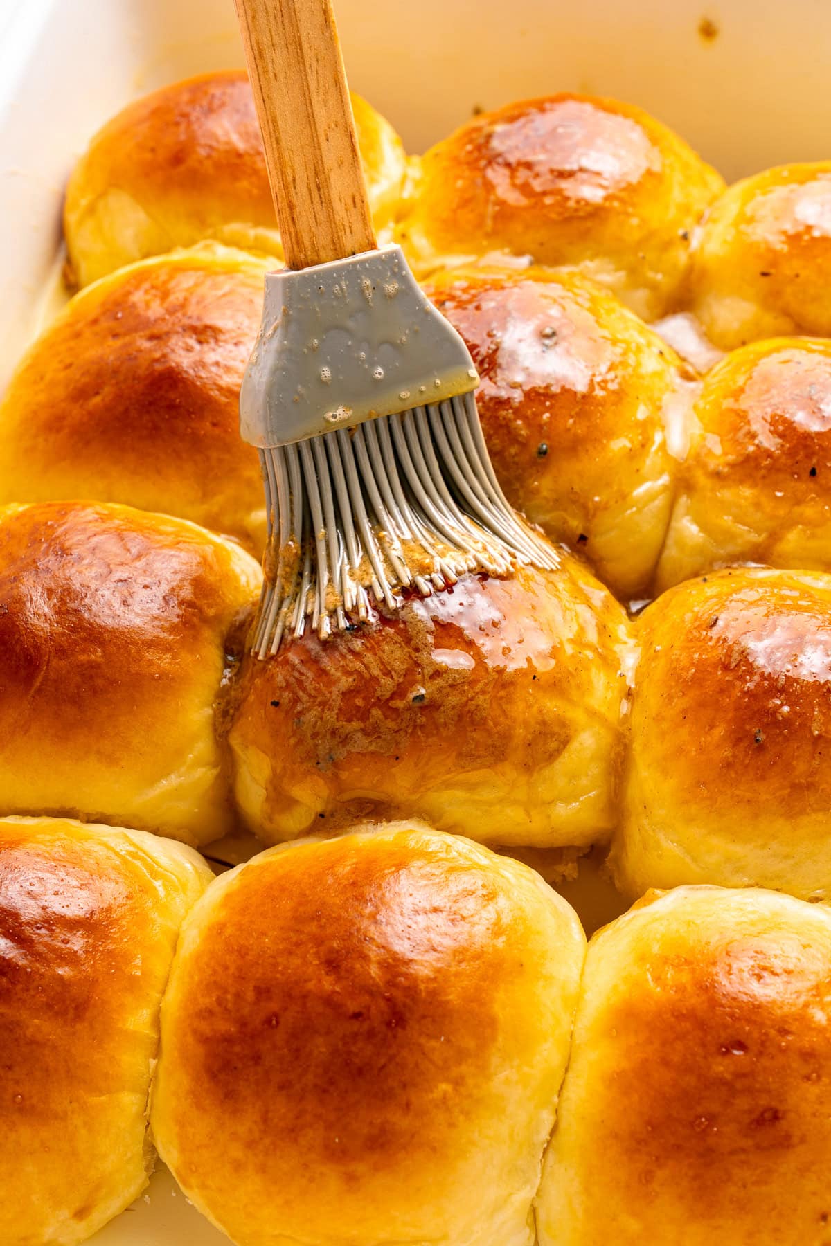 Brushing melted butter over hawaiian rolls.